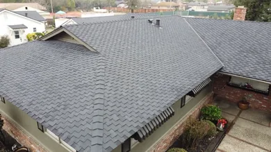 Aerial view of a newly shingled hip roof over a brick and siding home