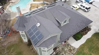 Aerial view of a completed gray composition shingle roof on a two-story home with a rooftop solar array